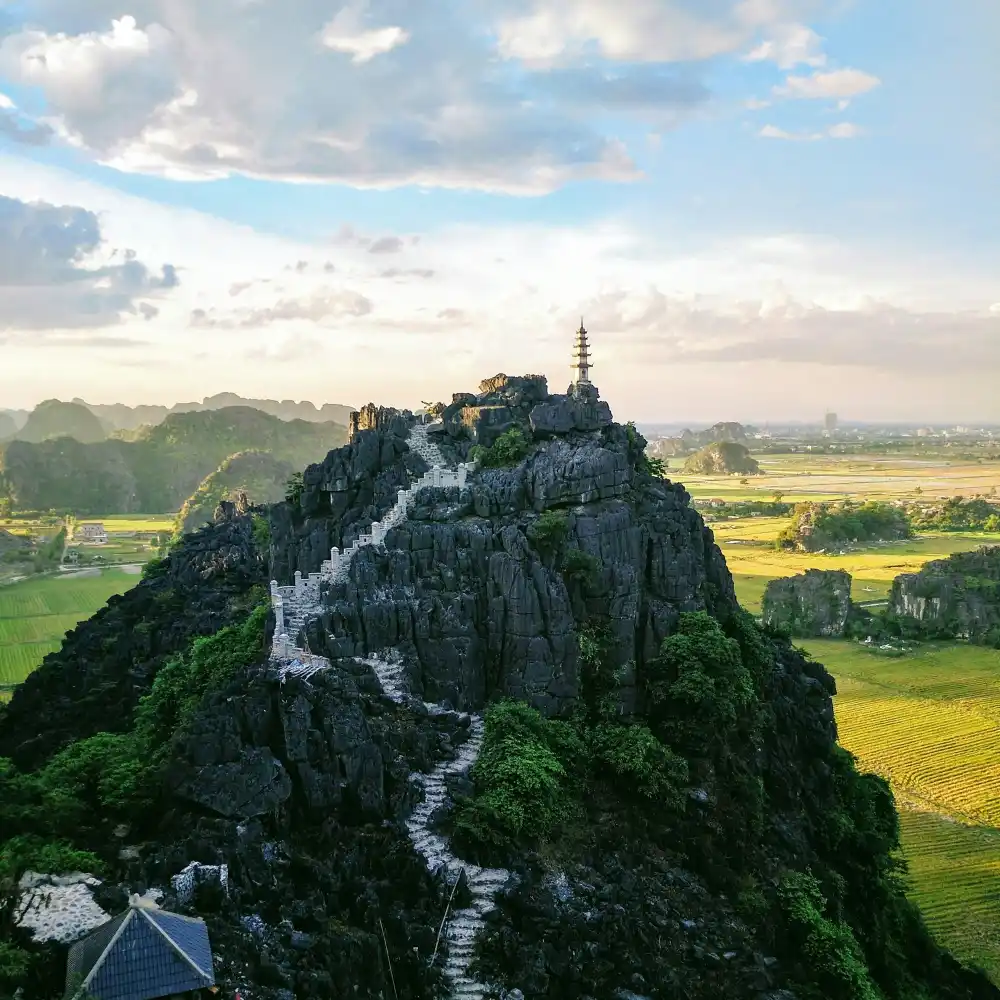 Lối bậc đá uốn lượn lên đỉnh Hang Múa, phía xa là đồng lúa và núi đá vôi