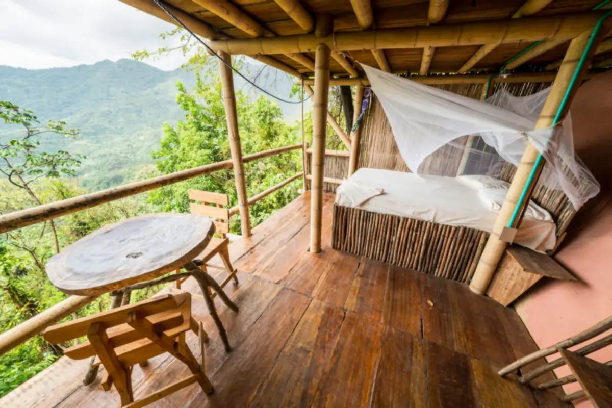 Hiên sàn gỗ dưới mái tre của homestay nguyên căn Ninh Bình, giường buông màn tuyn nhìn ra đồi núi xanh